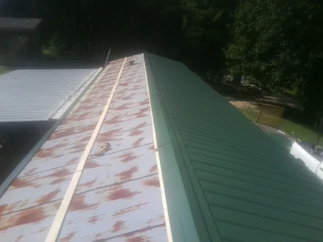 Old rusted panels beside newly installed green metal roofing — Wind Damage Roof Repair by Roofing Brothers in Crimora