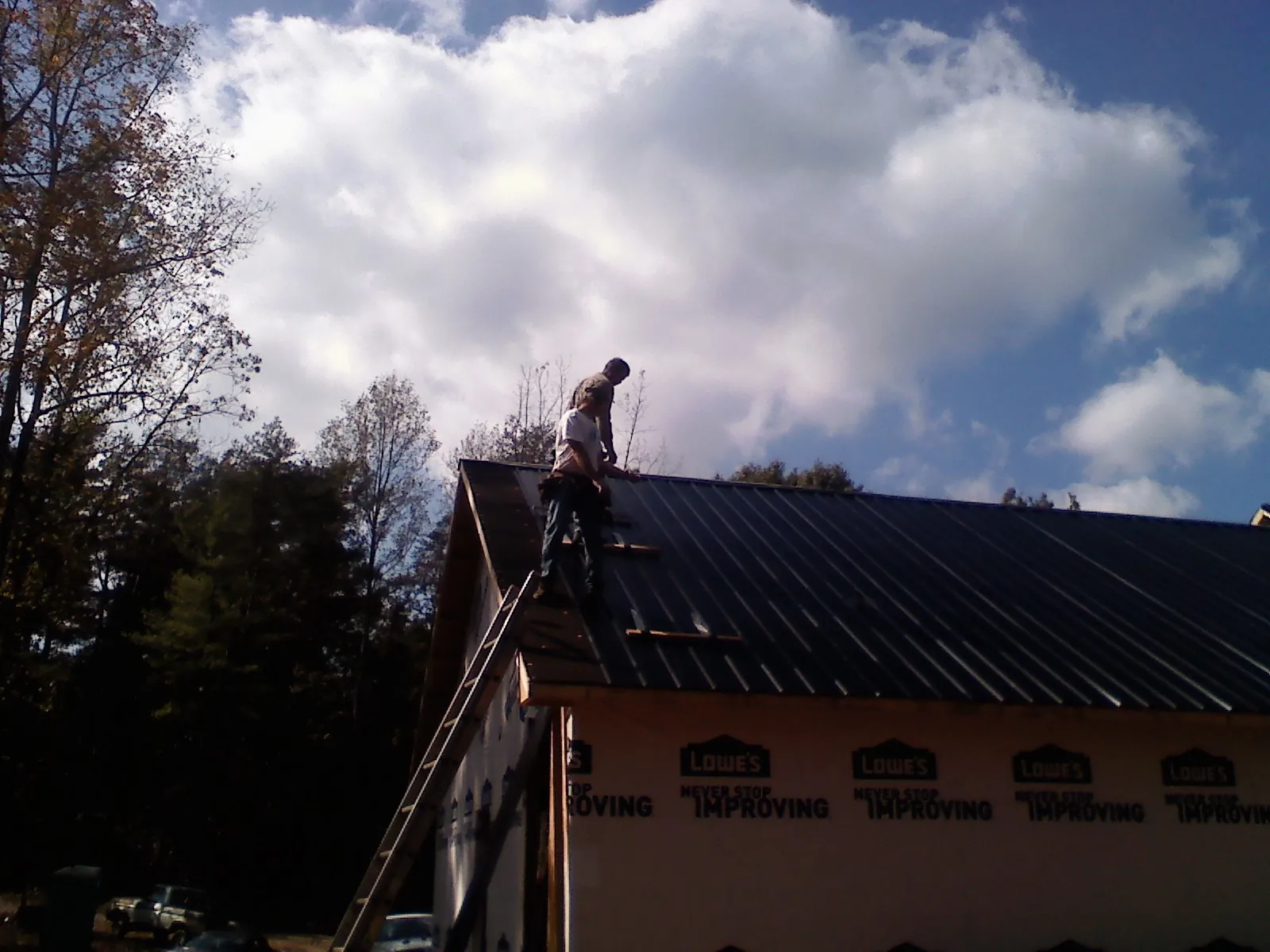 Roofer fastening dark metal panels high against a cloudy sky, from a Roof Inspection job in Crimora