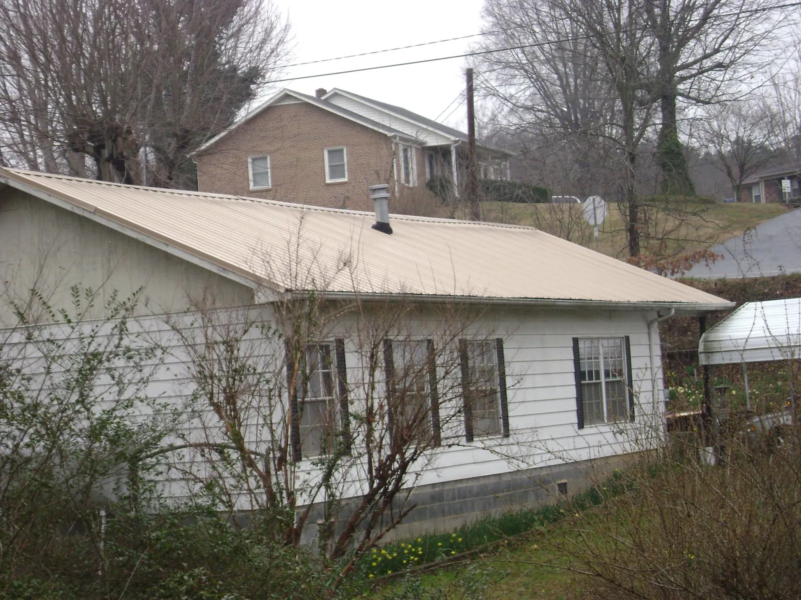 Tan metal roof on a white sided house set into a hillside — Commercial Roofing by Roofing Brothers in Crimora